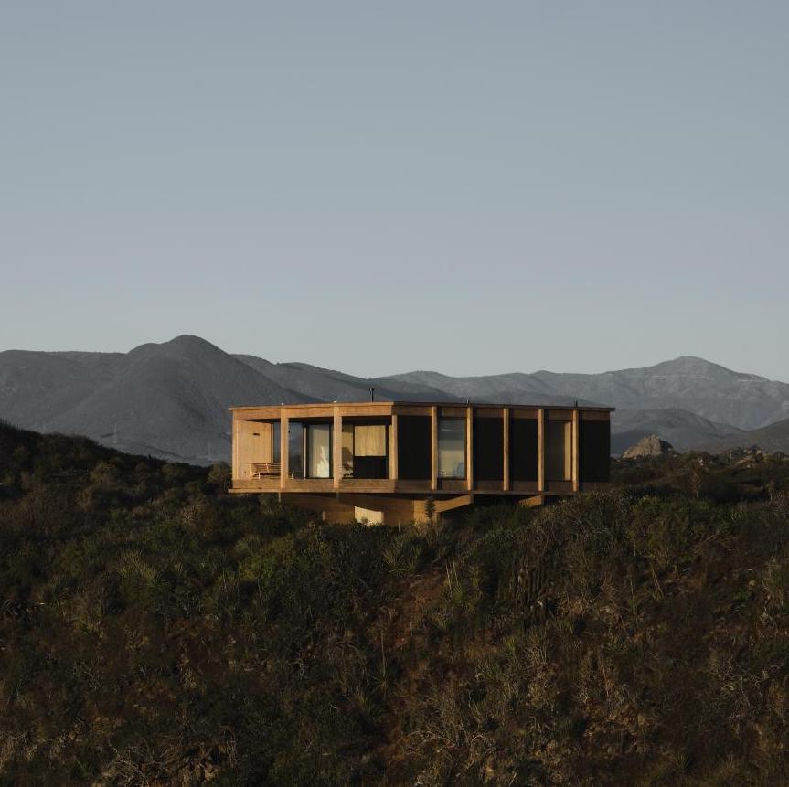 Modern wooden house overlooking scenic mountain landscape, eco-friendly architecture, and large glass windows.