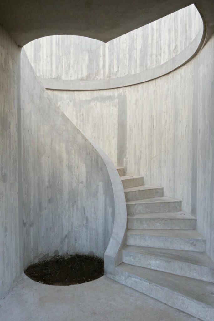 Detailed close-up of the sculptural helical staircase at CR House, emphasizing its smooth concrete finish and artistic curvature