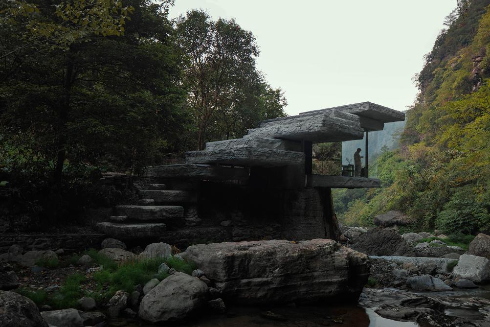 Glass-walled room with views of forest and cliffs beneath stone steps