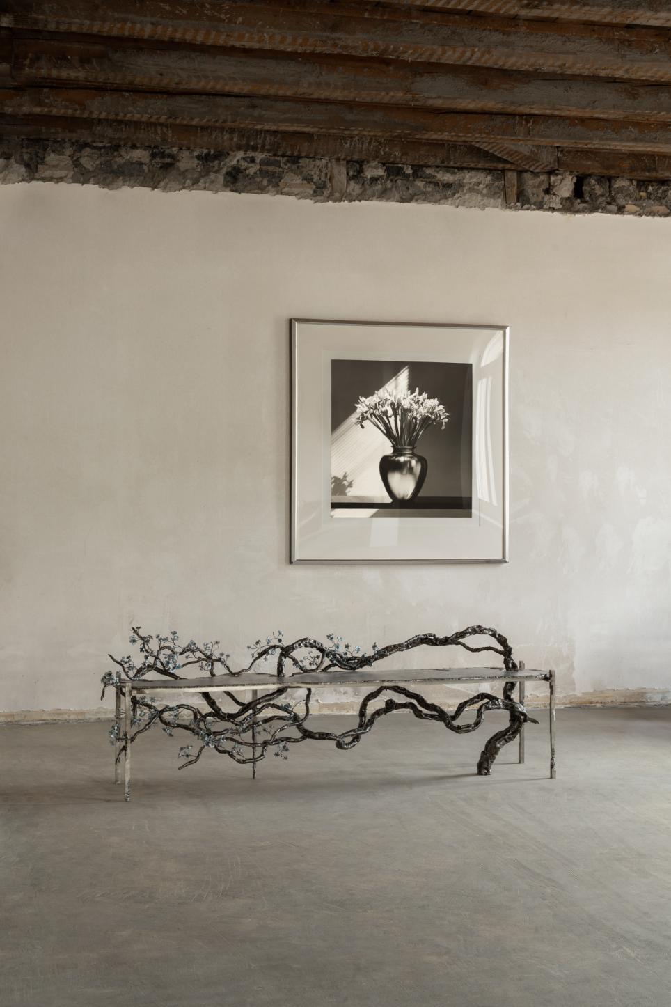 Branch sculpture on metal bench in minimalist art gallery.