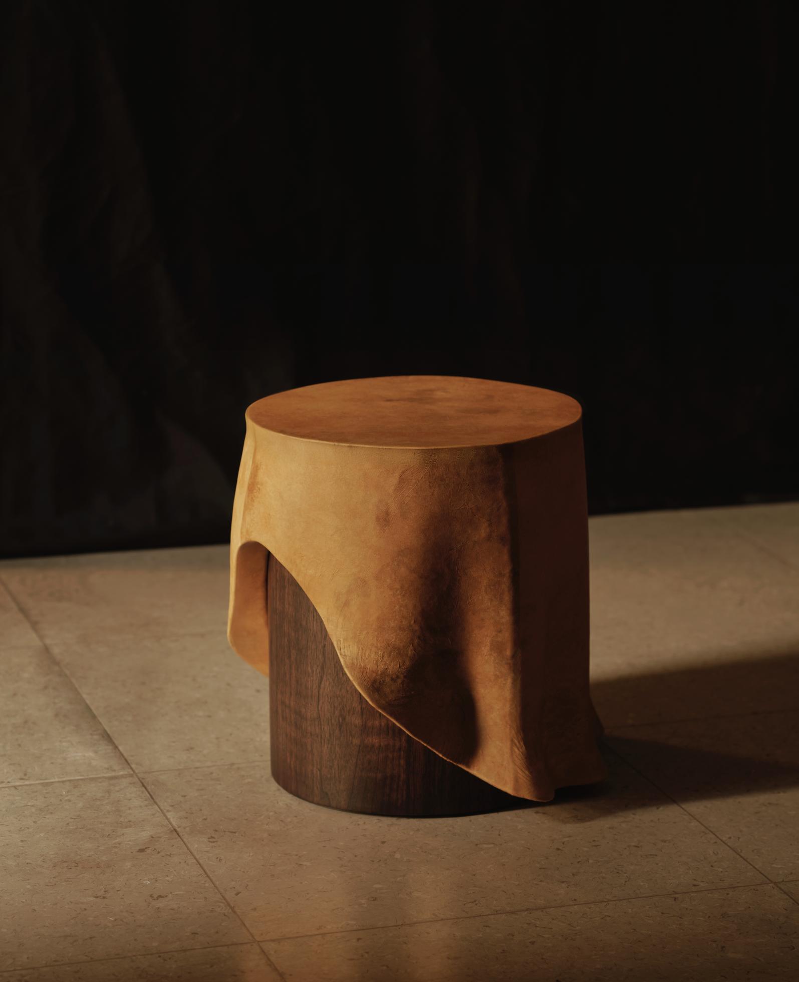 Rustic wooden stool with a leather piece draped over it, highlighting natural materials and craftsmanship.