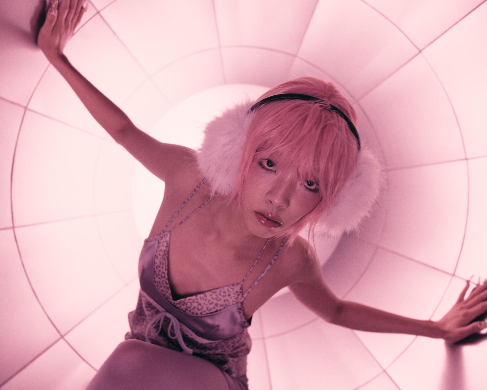 Vibrant pink-haired woman with fluffy earmuffs inside a futuristic tunnel, emphasizing modern fashion and creative photography.