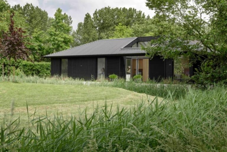 A serene senior home by i29 supports independent family living Modern black house surrounded by lush green trees and grass.