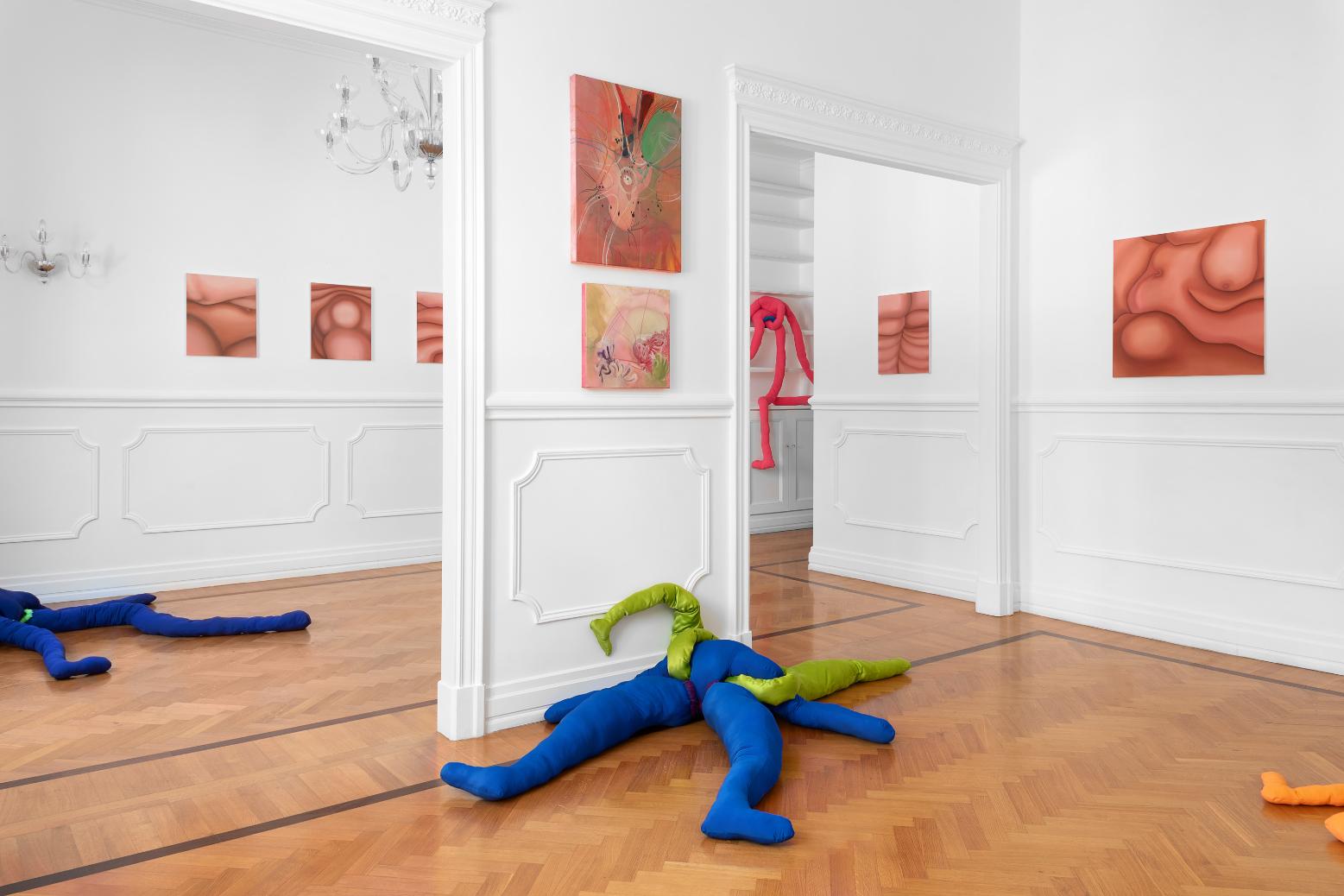 Colorful fabric sculptures in an art gallery featuring abstract paintings and modern interior design.