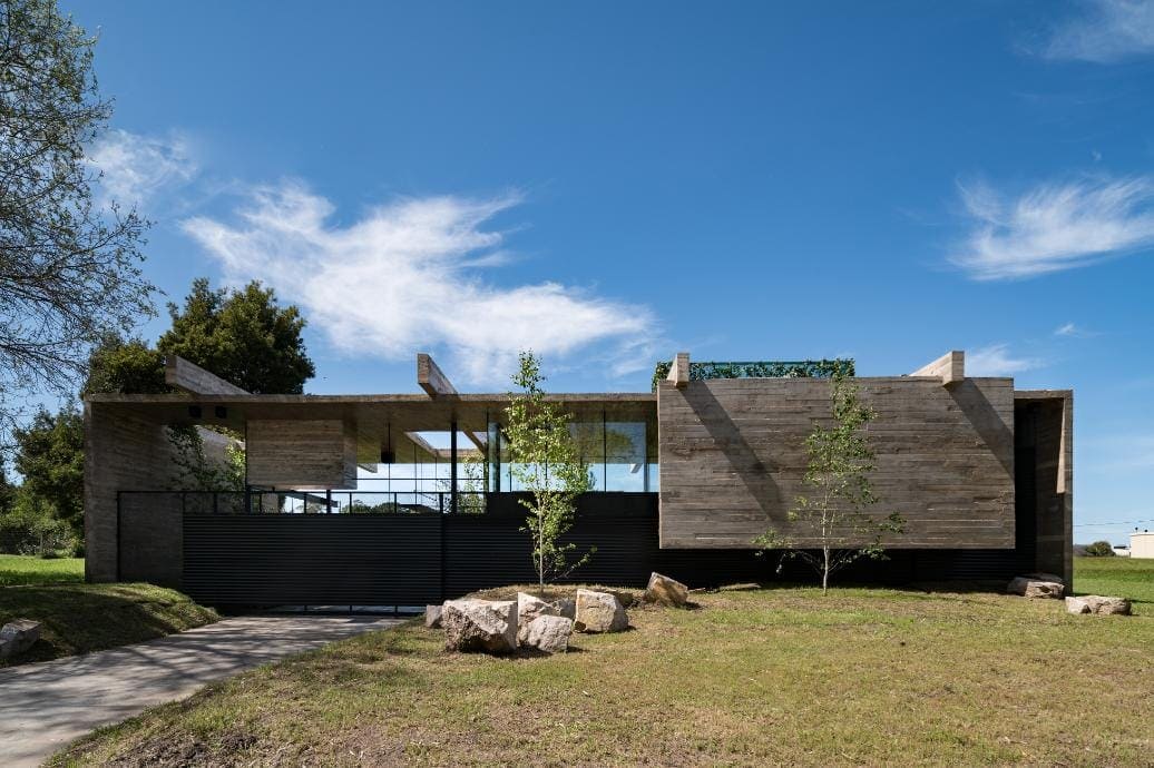 Modern minimalist house with concrete and wood exterior design, landscaped yard, and blue sky.