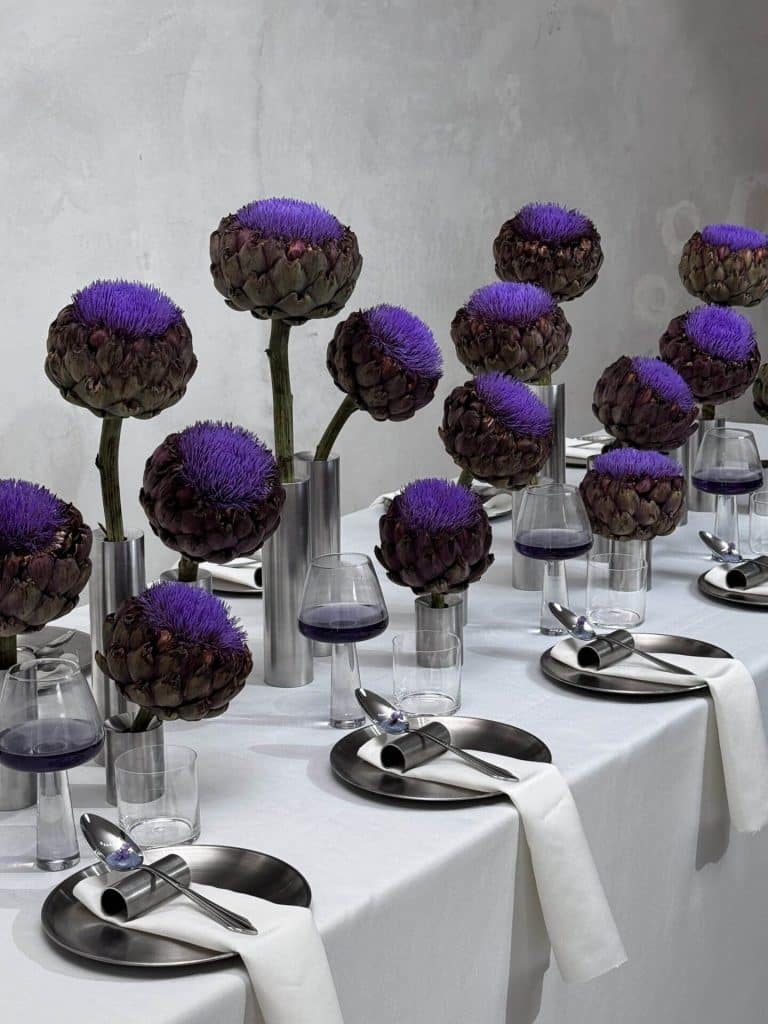 Idan Gilony creates immersive and emotional sensory experiences Vibrant artichoke flower centerpieces with purple blooms on a modern table setting for elegant dining.