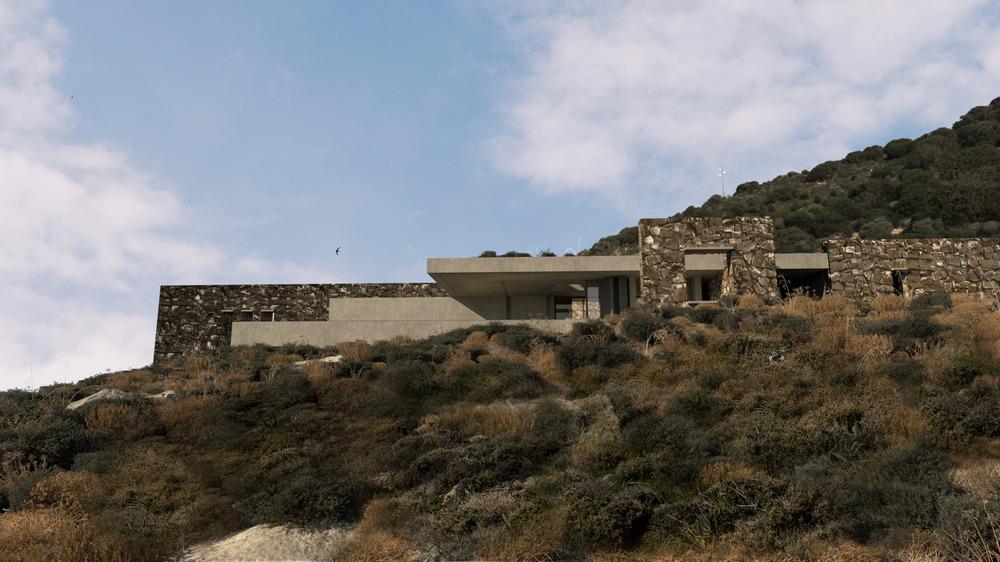 Stone and concrete façade of the residence with deep openings designed for passive cooling