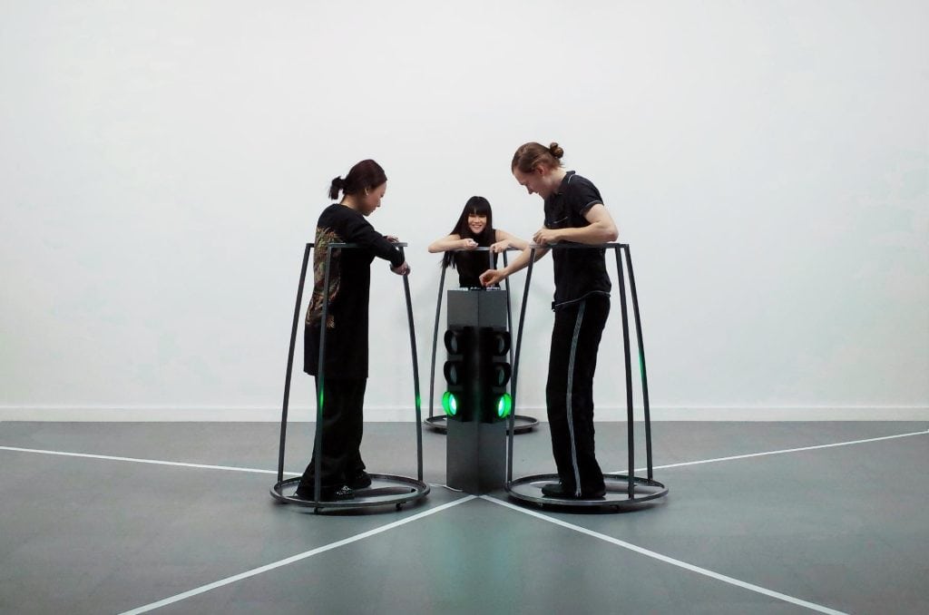 Three participants moving across a triangular field while controlling each other’s paths through remote devices.