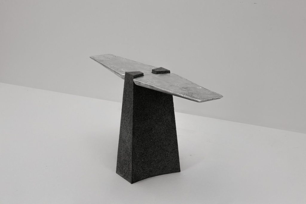 Cast metal console balanced on a carved volcanic stone base