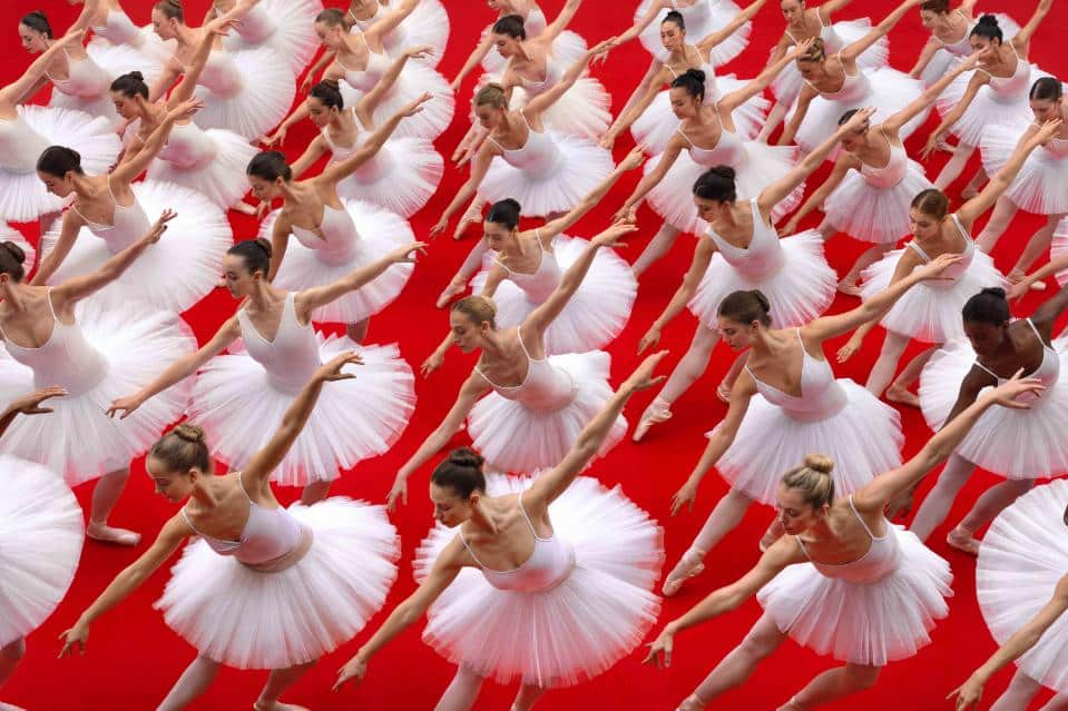 Overhead view of ballet dancers forming geometric patterns on a red carpeted floor.
