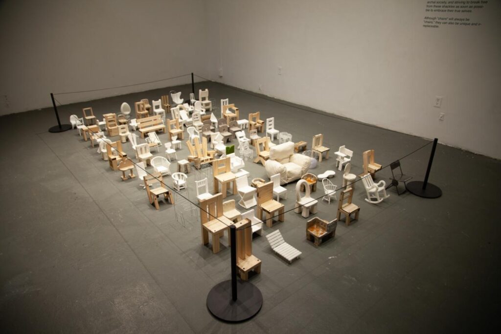 Installation view showing rows of uniquely formed chairs across the gallery