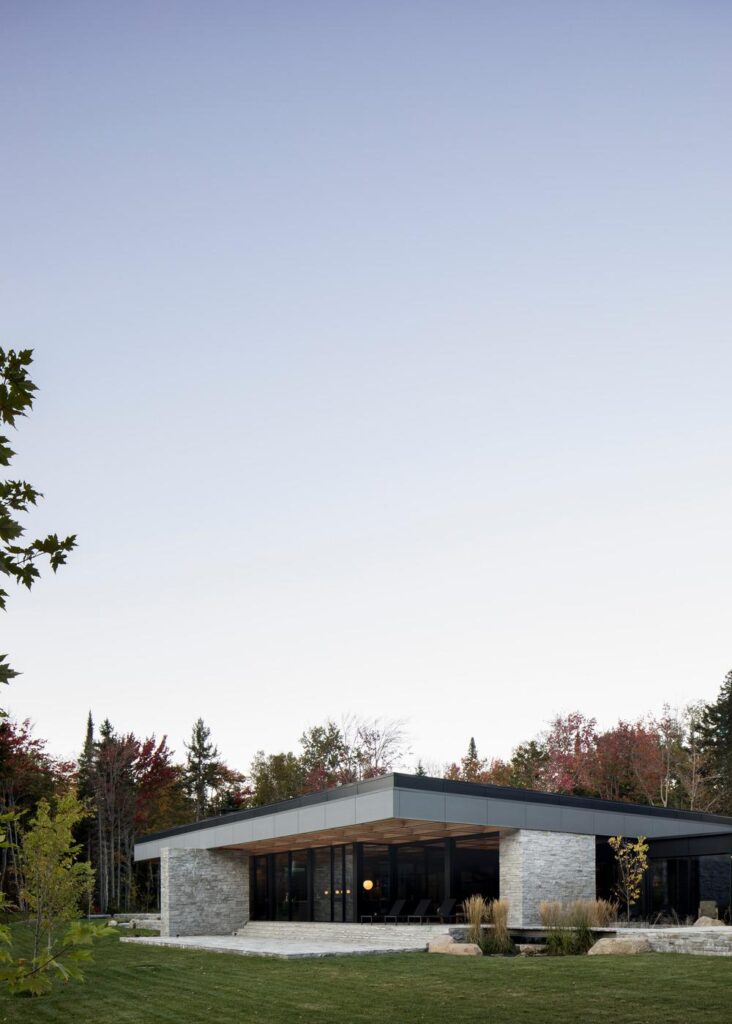 Exterior view of the house with timber roof extending toward the lake amid dense forest