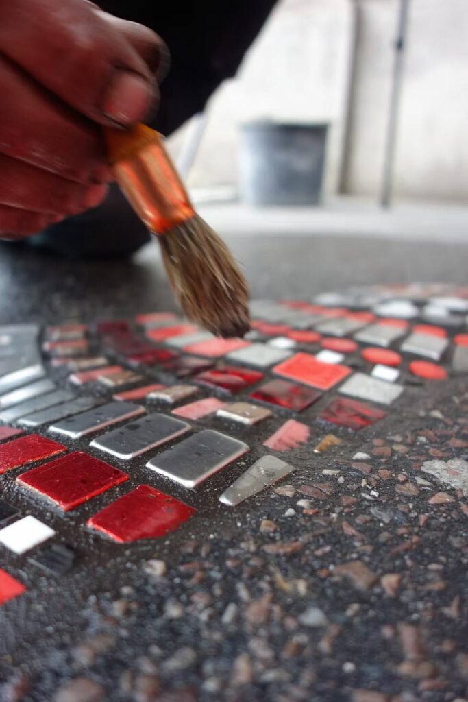 Ememem’s ceramic “flacking” repair filling a cracked sidewalk with multicoloured mosaic tiles