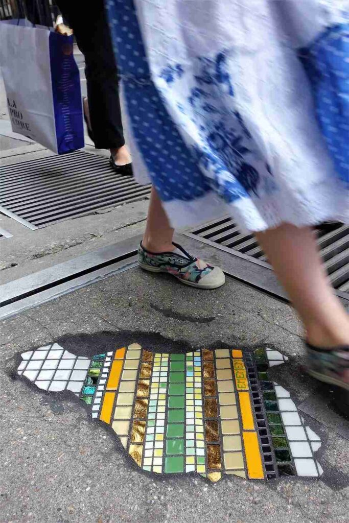 Flacking intervention in a curbside crack, with colourful tiles contrasting the bitumen