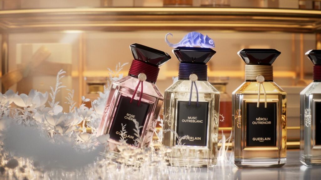 Guerlain perfume bottles arranged among white paper flowers with an origami chameleon above