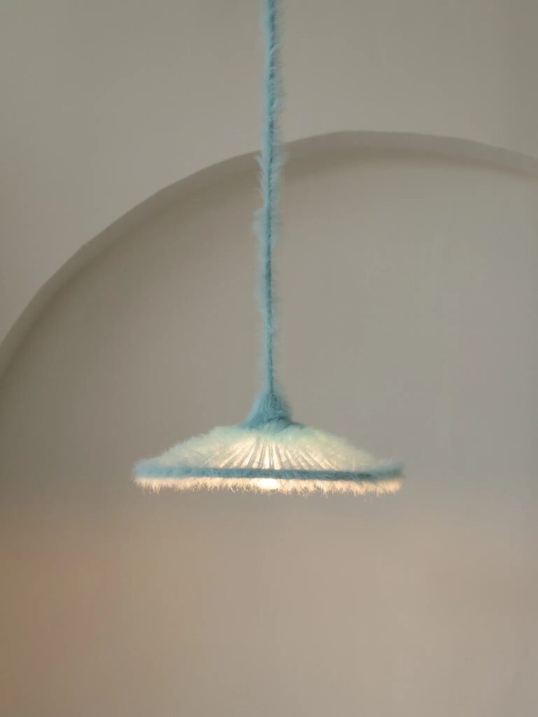Blue hand-knitted pendant lamp glowing in front of a white arched wall