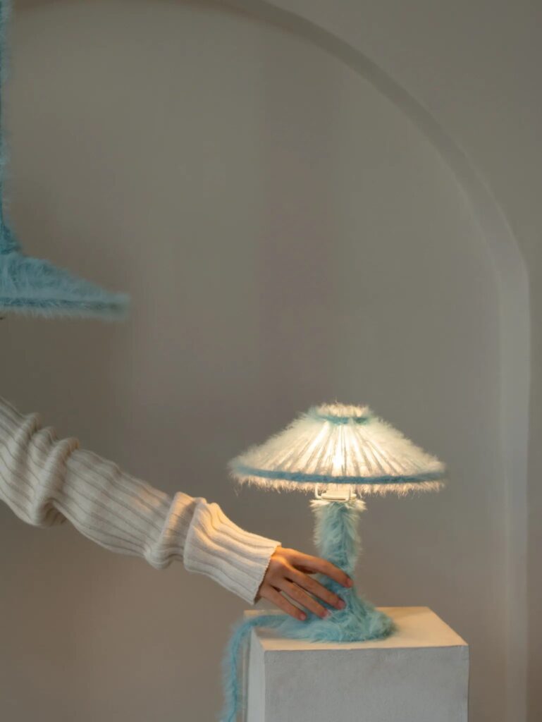Hand switching white inline control on blue furry lamp cable beside white pedestal