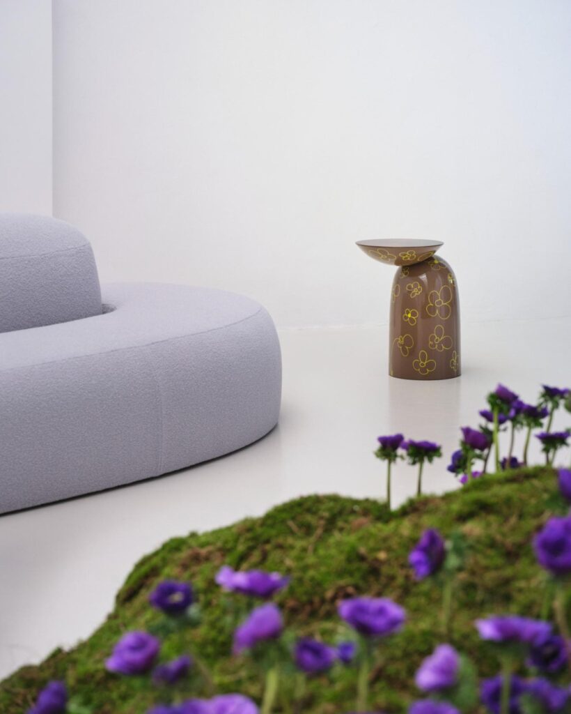 Detail of the curved sofa beside a brown side table with floral graphics and purple flowers