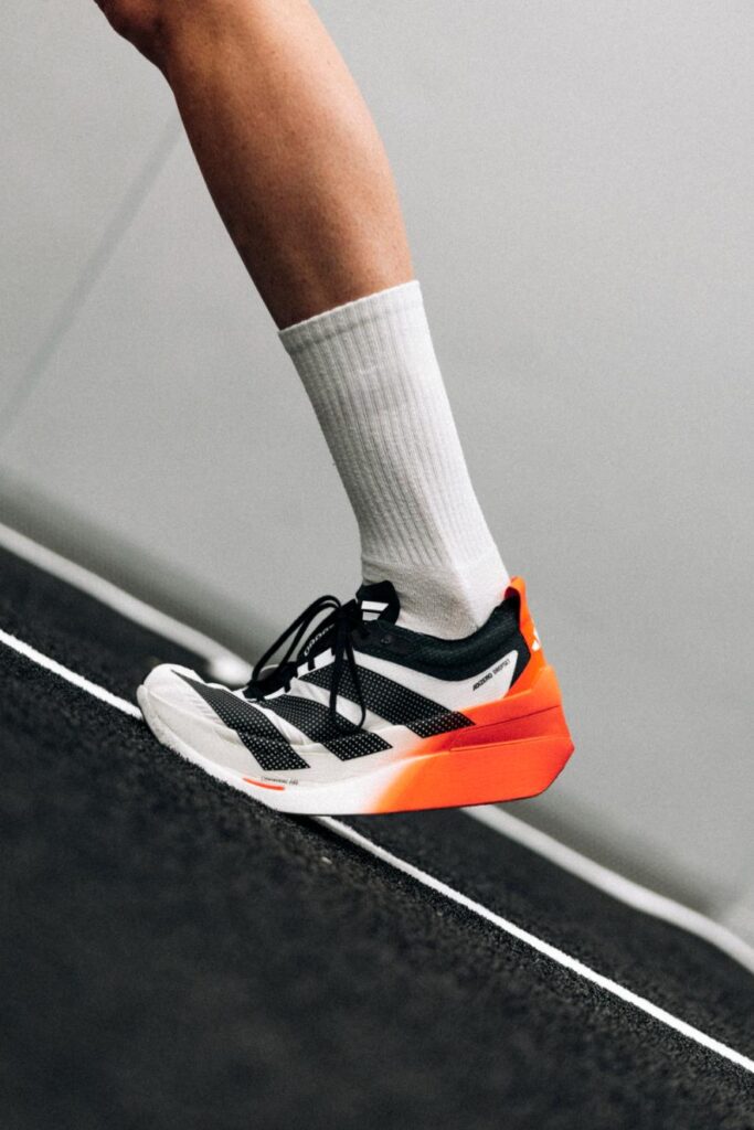 Runner wearing adidas Adizero Dropset Elite on indoor track, showing side profile and orange heel geometry