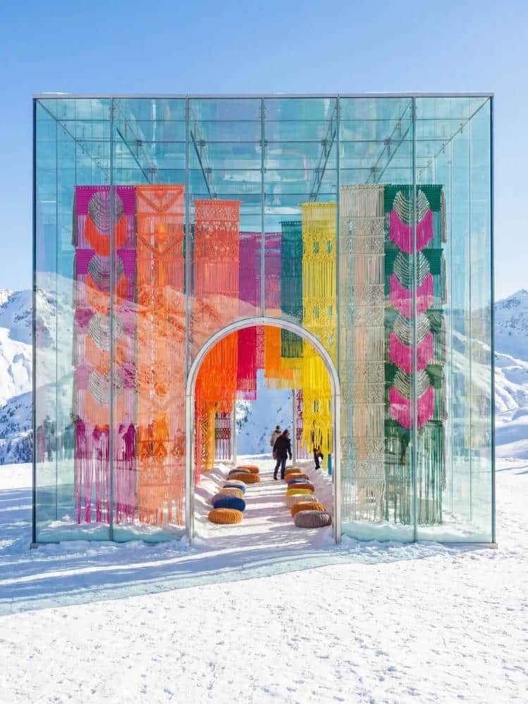 Milla Novo’s knotted textile panels hang inside a glass cube pavilion in the Alps with an arched entrance