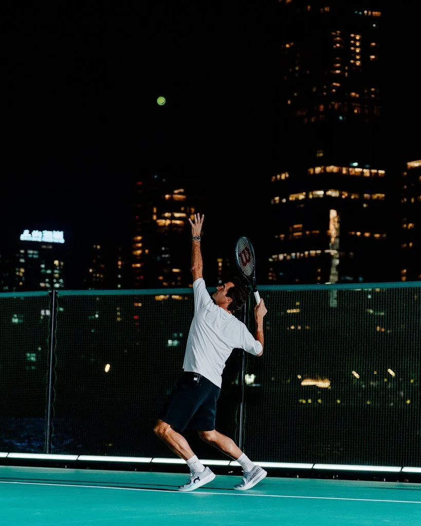 Roger Federer serves a tennis ball on On floating tennis court against the Shenzhen skyline at night